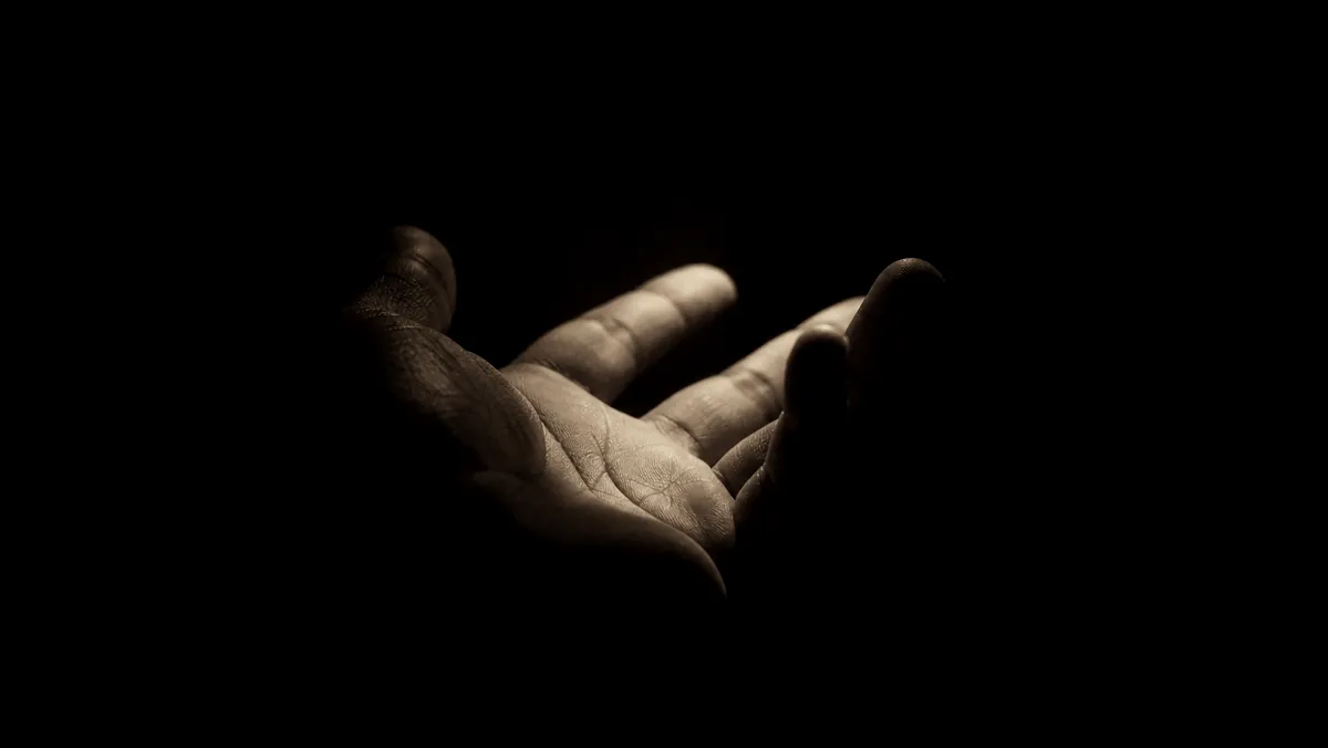 An open palm held in darkness beneath a small warm light.