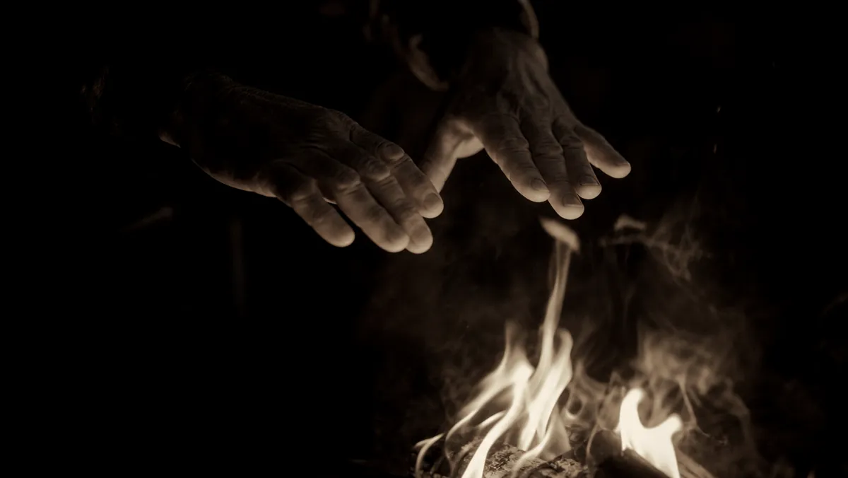 Hands moving above an open fire at dusk.